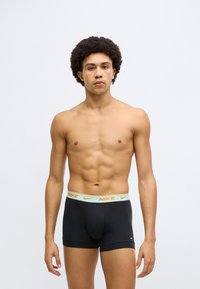 Mustad poksipüksid, millel on heleroheline ja oranž vöökoht, millel on Nike logo. Siledat tekstuuri, hästi istuv disain ja keskmise pikkusega lõige.