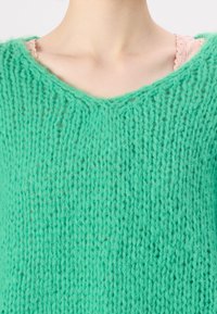 Pull tricoté vert menthe avec un col en V, fabriqué en laine douce présentant un motif texturé et légèrement ajouré.