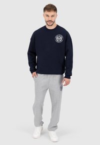 Set di felpa blu marina e pantaloni tuta grigi. La felpa presenta un logo rotondo sul petto; i pantaloni hanno un logo sulla coscia. Entrambi sono realizzati in cotone.