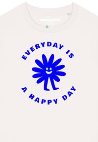 Das weiße T-Shirt verfügt über ein blaues, blumenähnliches Grafikdesign mit einem lächelnden Gesicht und grünen Augen, umgeben von dem Text „JEDER TAG IST EIN GLÜCKLICHER TAG.“