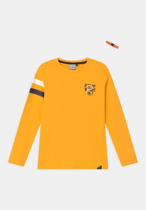 Gelbes Langarmshirt mit Rundhalsausschnitt, schwarzen und weißen Streifen am linken Ärmel und dem Schriftzug "Rise Up Without Limits" auf der Brust.