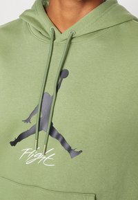 Felpa verde con una texture liscia, caratterizzata da una grafica nera della silhouette Jordan e il testo "Flight" sul davanti. Stringhe coordinati in verde.