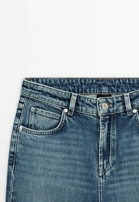 Farkkushousut keskipunaisella sinisellä värillä, suoran leikkauksen omaavat. Varustettu nappisulkemisella, sivutaskuilla ja erottuvalla tikkauksella. Suova tekstuuri, klassinen muotoilu.