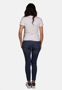 T-shirt bianca a maniche corte, design aderente, abbinata a jeans skinny blu scuro. Stile minimalista senza motivi o grafiche visibili.