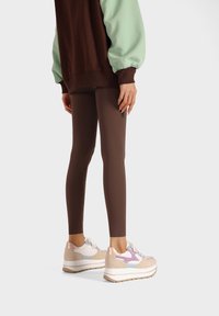 Legging bruns associés à un sweatshirt surdimensionné marron et menthe. Les chaussures présentent un design léger multicolore en beige, lavande et blanc.