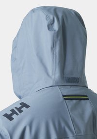 Giacca impermeabile azzurro chiaro con cappuccio, logo nero "HH" sulla spalla e banda riflettente sulla parte superiore della schiena.