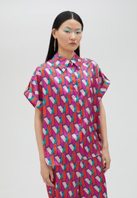 Short-sleeve shirt with a button-up collar, made of silky fabric featuring a geometric pattern in pink, red, purple, and green hues.