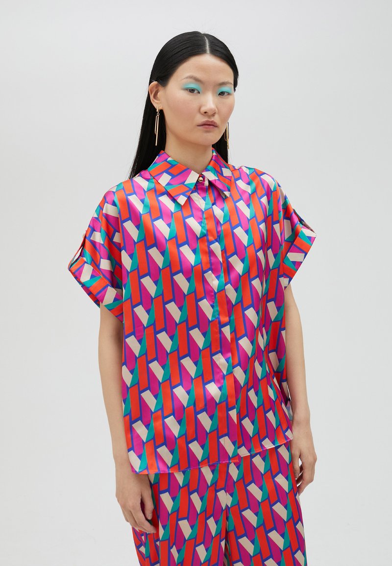 Short-sleeve shirt with a button-up collar, made of silky fabric featuring a geometric pattern in pink, red, purple, and green hues.