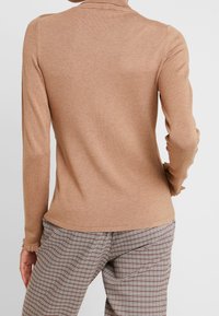 Haut beige à manches longues avec un col montant et un léger volant aux poignets, associé à un pantalon taille haute à carreaux dans des tons neutres.