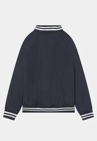 Granatowa kurtka bomberka z prążkowanym kołnierzem, białymi paskami na mankietach i dolnej krawędzi oraz gładkim, lekkim materiałem.