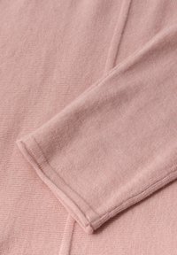 Tela de punto rosa con una textura suave, que presenta una superficie lisa y un detalle de manga plegada. Costuras prominentes a lo largo de los bordes.