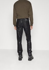 Svarta läderbyxor med en glänsande yta, figursydd design och två bakfickor. Bärs med en mörkbrun tröja och svarta skor.