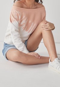 Mikina bez ramínek v růžovo-bílém tie-dye, z bavlněné směsi, měkká textura. Kombinováno s denimovými šortkami a bílými teniskami.