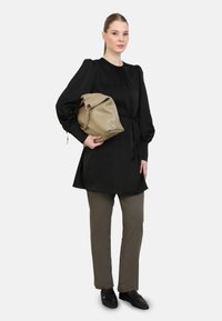 Black long-sleeve top with puffed shoulders, cinched waist; khaki trousers; model holding a beige leather bag with chain accents.