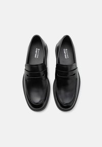 Mocasines de cuero vegano negro con un diseño minimalista, que cuentan con una tira elevada en el vampiro y un acabado suave.