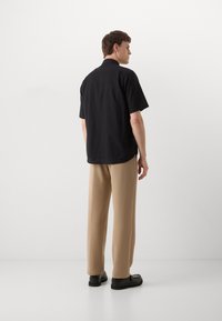 Maglietta nera a maniche corte con vestibilità comoda, abbinata a pantaloni beige. La maglietta presenta un colletto classico e spacchi laterali. Scarpe nere.