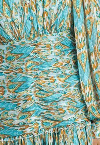 Vestido floral con un patrón en turquesa, naranja y crema. Confeccionado en tejido ligero con textura fruncida y detalle de dobladillo con volantes.