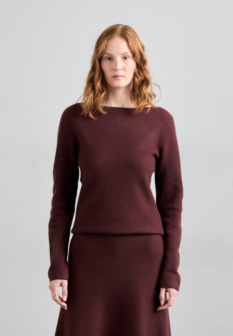 Burgunderfarbener Wollpullover mit langen Ärmeln und weiter Bootskragen, kombiniert mit einem passenden taillierten Rock. Weiche Textur und minimale Designelemente.