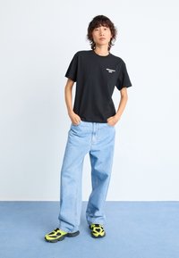 Black cotton t-shirt with short sleeves and a printed detail, paired with light blue denim jeans and black/yellow sneakers.