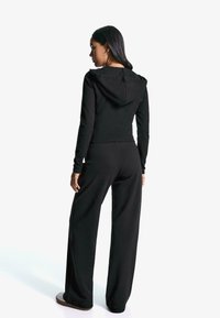 Čierna mikina s kapucňou a zodpovedajúce široké nohavice vyrobené z mäkkej látky. Mikina má šnúrku na stiahnutie a priliehajúce manžety.