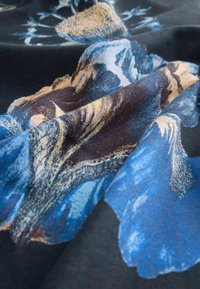 Audinio su gėlių raštu, turinčiu mėlynų ir auksinių akcentų ant tamsaus fono, pabrėžiančio sklandžią tekstūrą ir išsamius detalizavimus.