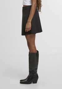 Falda negra plisada combinada con botas altas de imitación cuero negro hasta la rodilla, con punta afilada y tacón grueso. Textura suave, diseño casual.