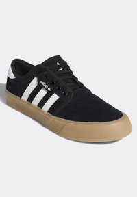 Svarta mockasko Pär med tre vita ränder, svarta snören och en sula av gummirubber. Har vadderad krage och logotypdetalj på sidan.