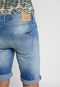 Ljust blå denimshorts med uppvikta fållar, med en tan läderetikett med "BLEND" på baksidan. Två bakfickor med sömnadsdetaljer.