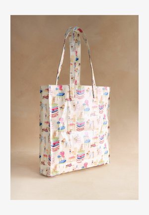 Krém színű táska hosszú fogantyúkkal, színes kutyás nyomatokkal, halmozott párnákkal és kis bútor darabokkal díszítve.