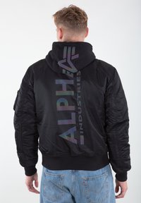 Black bomber jacket featuring a hood, ribbed cuffs and hem, with a large iridescent logo on the back. Made of smooth, padded material.