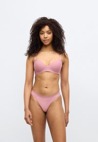 Σετ ροζ εσωρούχων που περιλαμβάνει ένα μαλακό επενδεδυμένο σουτιέν με ρυθμιζόμενους ιμάντες και τόνγκ που ταιριάζει με υφή στη μέση. Απαλό υλικό, αδιάκοπος σχεδιασμός.