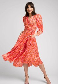 Czerwona i różowa wzorzysta sukienka kopertowa z długimi puff sleeves, związaną w talii i płynącym dołem, uszyta z lekkiego materiału.