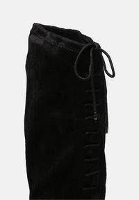 Černé semišové kotníkové boty s jemnou texturou, s krajkovým detailem na boku a nařaseným vrchem utaženým pomocí šňůrky.