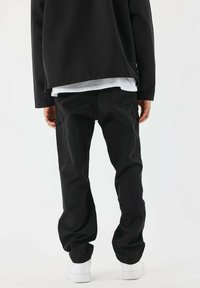 Pantaloni cargo neri con una vestibilità rilassata; presentano tasche laterali, un tessuto resistente e una leggera caduta. Indossati con un lungo giaccone nero e scarpe bianche.