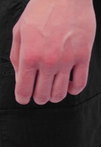 Zbliżenie na dłoń z widocznymi żyłami i zmarszczkami, o jasnym odcieniu skóry; tło stanowi ciemna tkanina z logo Adidas.