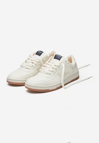 White leather sneakers with perforated toe, rubber sole, and cream accents. Features white laces and a small brand tag on the tongue.