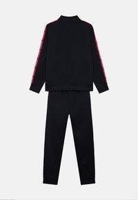 Ensemble de survêtement noir comprenant une veste zippée avec un grand col et des accents rouges le long des manches, accompagnée d'un pantalon assorti avec des poignets.