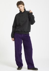 Pullover nero con colletto alto e bottoni, abbinato a pantaloni in corduroy viola a vestibilità ampia. Tessuto strutturato, stile casual.