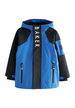 Lächelnder Junge trägt eine blau-schwarze Kapuzenjacke mit dem Text "Baker by Ted Baker" auf der Reißverschlussklappe vor einem einfarbigen grauen Hintergrund.