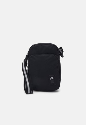 Kleine zwarte Nike crossbodytas met voorvak met rits en verstelbare zwarte band met witte strepen.