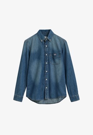 Camisa de mezclilla azul claro con mangas largas, frente abotonado, cuello con puntas y un bolsillo en el pecho. Presenta un ligero desvanecimiento y un dobladillo curvado.