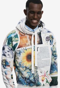 Hoodie med hætte har et collage af livlige mønstre og farver, herunder blomster- og naturbilleder, med en hvid snor og manchetter.