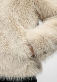 Faux fur sweater i creme, der har en tekstureret, fluffy overflade og skjulte lommer med en sort stofkant forneden.