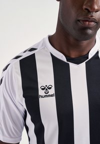 Zwart-wit gestreept sportshirt met korte mouwen, een V-hals ontwerp en het "hummel" logo aan de linkerkant van de borst.