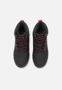 Zwarte schoenen met een gladde, matte afwerking. Voorzien van rood en zwart gemarmerde veters, versterkte veteropeningen en rode trekstrips bij de hiel.