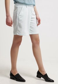 Ljusblå skräddarsydda shorts med slät front, två sidofickor och fållade kanter. Bärs med svarta slip-on skor. Slät textilfinish.