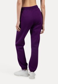 Lilla fleece sweatpants med elastisk talje og manchetter; har en afslappet pasform og glat tekstur; parret med hvide sportsko.