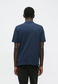 Polo-shirt bleu marine en coton, avec un design à manches courtes et un col classique. Simple, couleur unie sans motifs visibles.