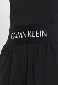 Black skirt with wide elastic waistband featuring white "CALVIN KLEIN" logo text in uppercase letters.