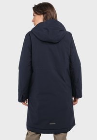 Langer, marineblauer Mantel mit Kapuze, aus wasserdichtem Material. Er hat einen geraden Schnitt und ist knielang, mit Seitentaschen und einem dezenten Logo.